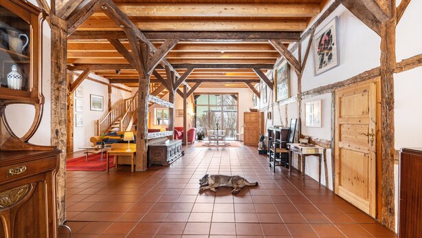 Une pièce spacieuse avec un sol carrelé, des poutres en bois, un chien allongé sur le sol et divers meubles, notamment une table et des chaises.