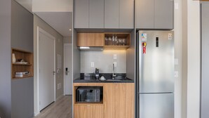 Et kompakt køkken med indbygget mikroovn, et rustfrit stål køleskab og en træhylde med glas.