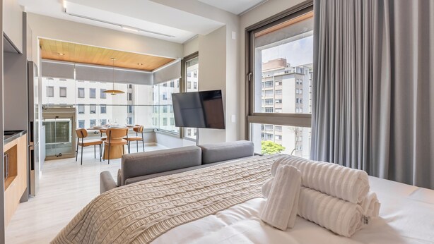 Et moderne hotelværelse med en stor seng, et fladskærms-tv, en balkon med spiseplads og udsigt over byen.