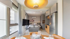 Et moderne hotelværelse med spiseplads, tekøkken og et fjernsyn i baggrunden.