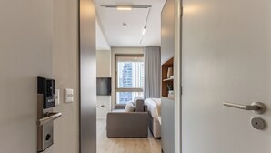 Et moderne hotelværelse med et fladskærms-tv, en sovesofa, trægulv og udsigt til bybilledet gennem vinduet.