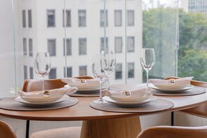 Ein Esstisch mit Geschirr, Gläsern und Servietten, mit Blick auf eine Stadtlandschaft durch große Fenster.