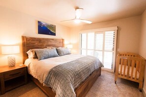 A bedroom with a bed, nightstands, a crib, a ceiling fan, and a window with blinds. - Basecamp Luxury Tahoe Keys waterfront retreat (South Lake Tahoe)