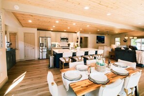 Una cocina amplia con armarios de madera, una isla central y un comedor con sillas blancas y una mesa de madera dispuesta para seis comensales.