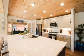 Una cocina moderna con techo de madera, armarios blancos, electrodomésticos de acero inoxidable y una isla de mármol.