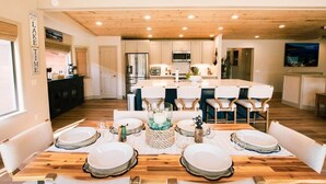 Una cocina moderna con armarios blancos, electrodomésticos de acero inoxidable y una mesa de comedor de madera para seis personas.