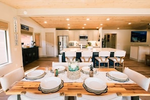 A modern kitchen with white cabinets, stainless steel appliances, and a wooden dining table set for six.