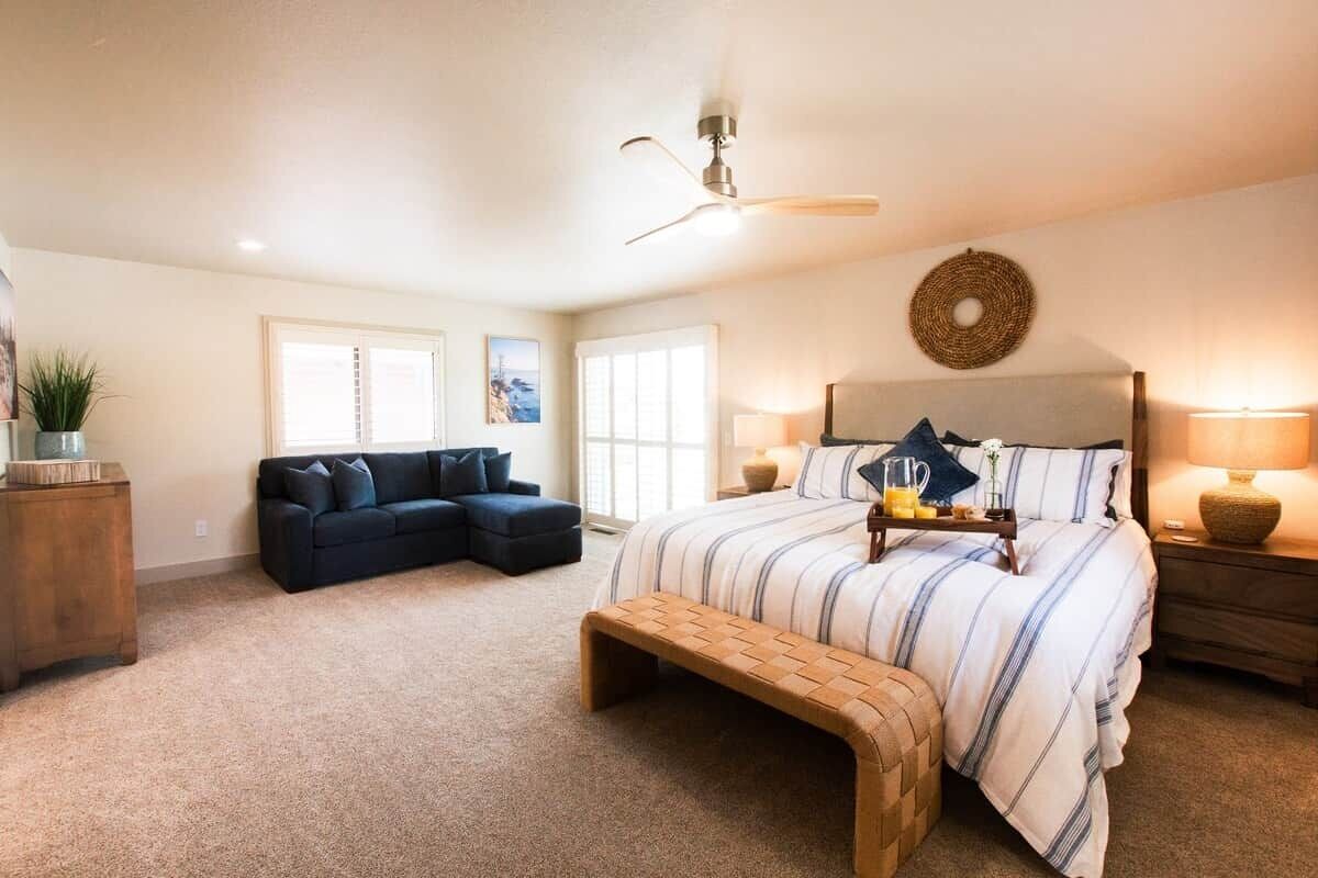 Une chambre à coucher comprenant un lit, un banc, une table de chevet, un ventilateur de plafond et une lampe fixée au mur.