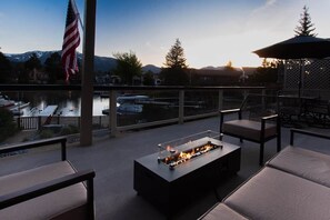 A balcony with a fire feature, outdoor furniture, and a view of a body of water and mountains.