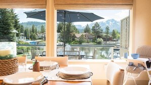 Un comedor con una mesa dispuesta para dos personas, con vistas a un lago y montañas al fondo.