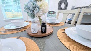 Une table à manger avec des salières et des poivrières, des bols blancs et un vase de fleurs.