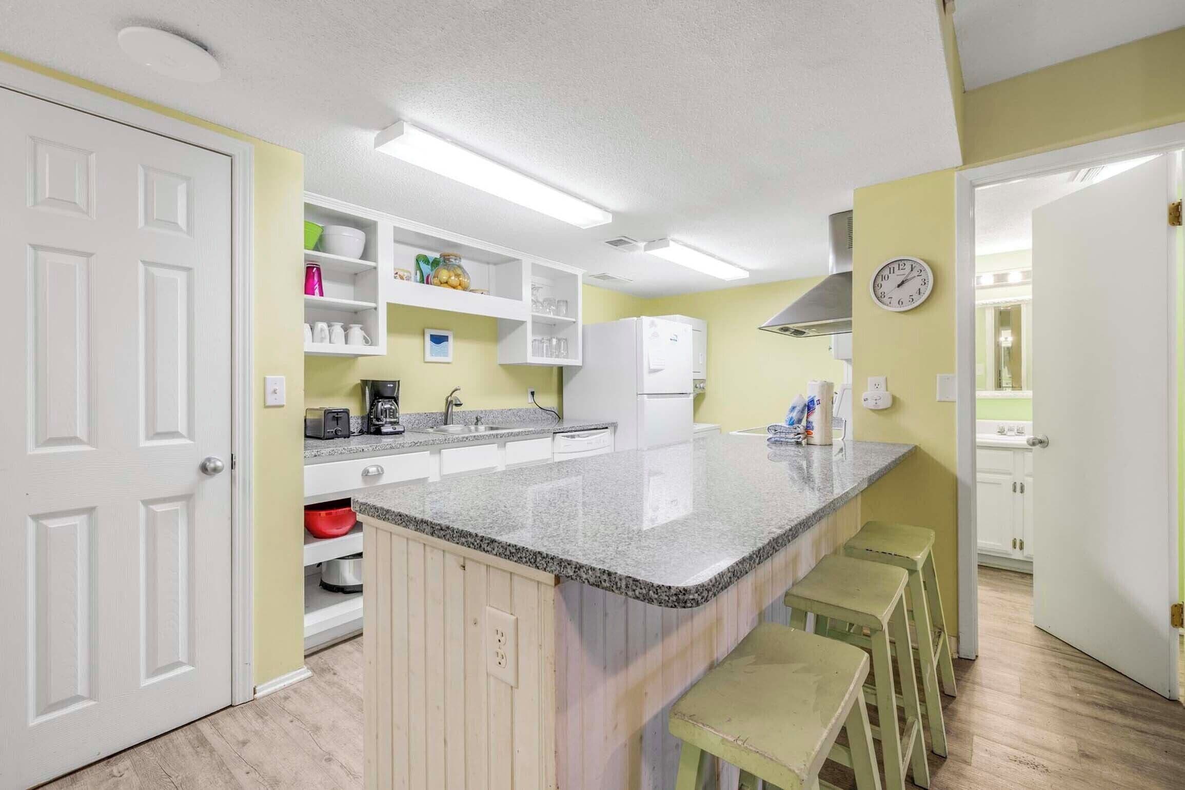 A kitchen with white cabinets, a granite countertop, and a built-in island with bar stools.