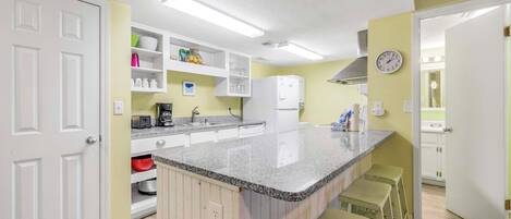 A kitchen with white cabinets, a granite countertop, and a built-in island with bar stools.
