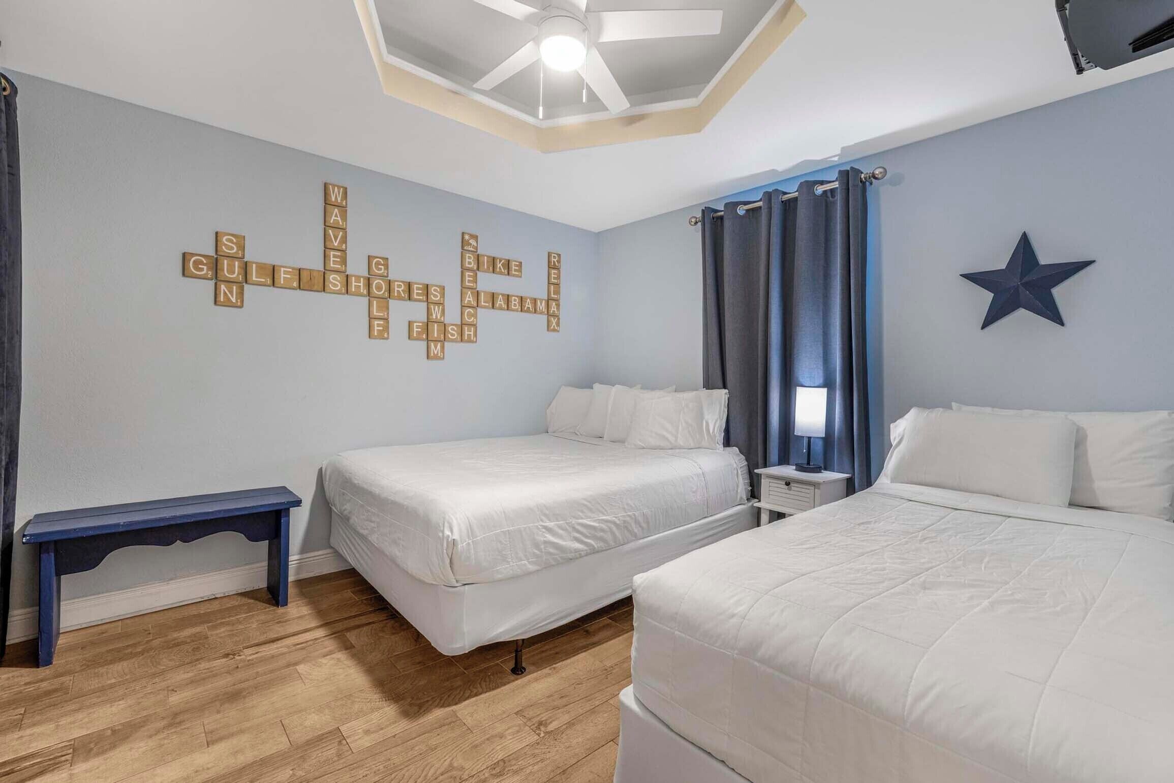 Un dormitorio con dos camas, un ventilador de techo, una pared con un crucigrama, una decoración de estrella y un banco.