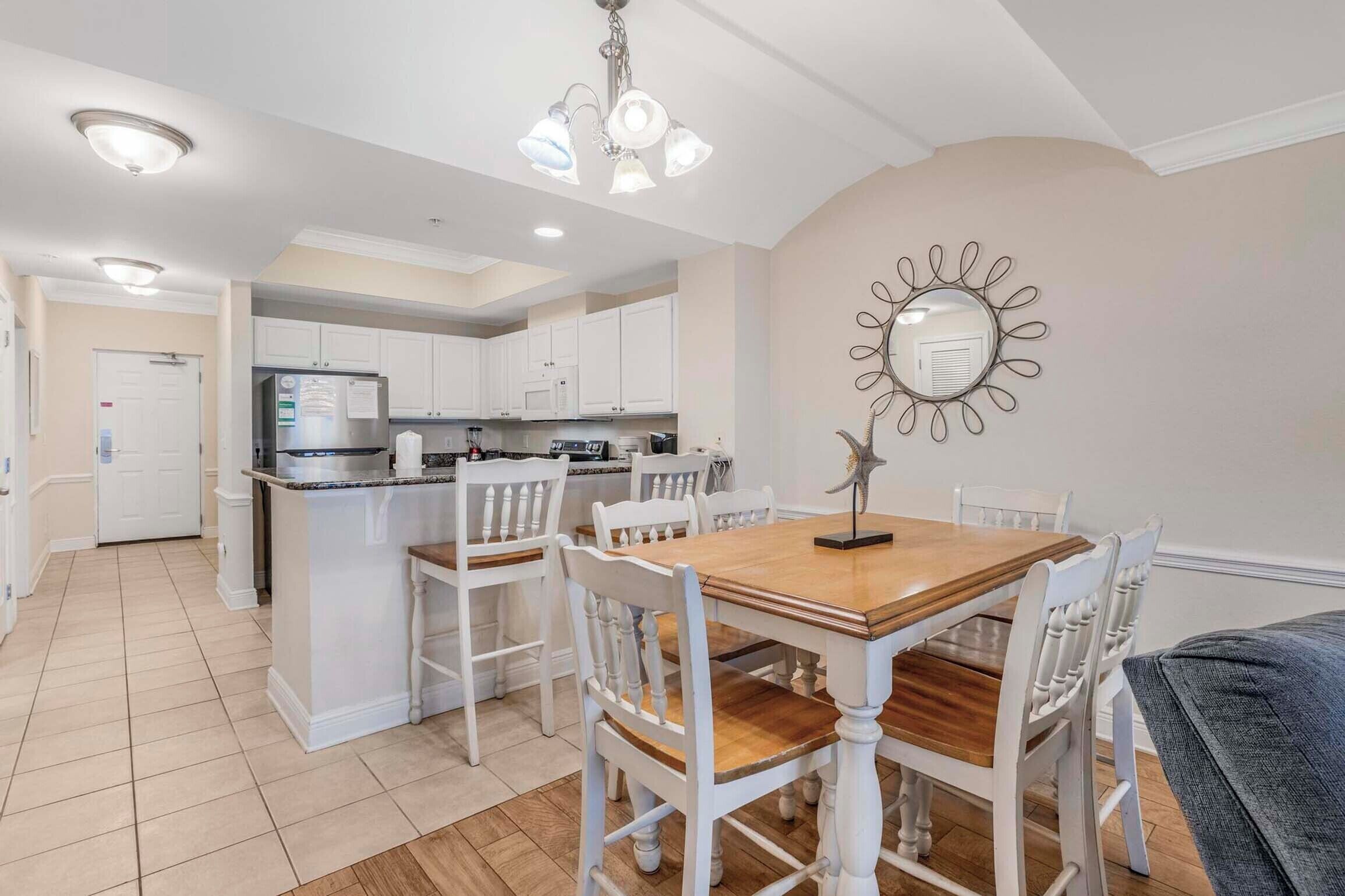 Una cocina moderna con muebles blancos, una isla central y un comedor con una mesa de madera y sillas blancas.