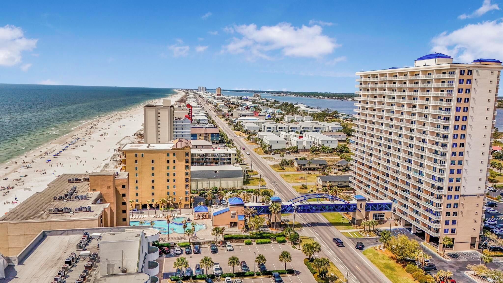 A coastal hotel with a beach view, multiple parking lots, and a swimming pool.