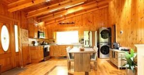 A wooden cabin interior with a kitchen, dining area, and a large window. - 2 bed, 2 bath, 1 min Walk to Downtown (Helen)
