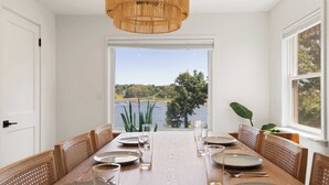 Une salle à manger avec une grande table dressée pour six personnes, une vue sur un lac et un luminaire suspendu.