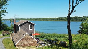 Une maison avec des fondations en pierre et un toit en pente, une terrasse avec des meubles d’extérieur et une vue sur un lac.