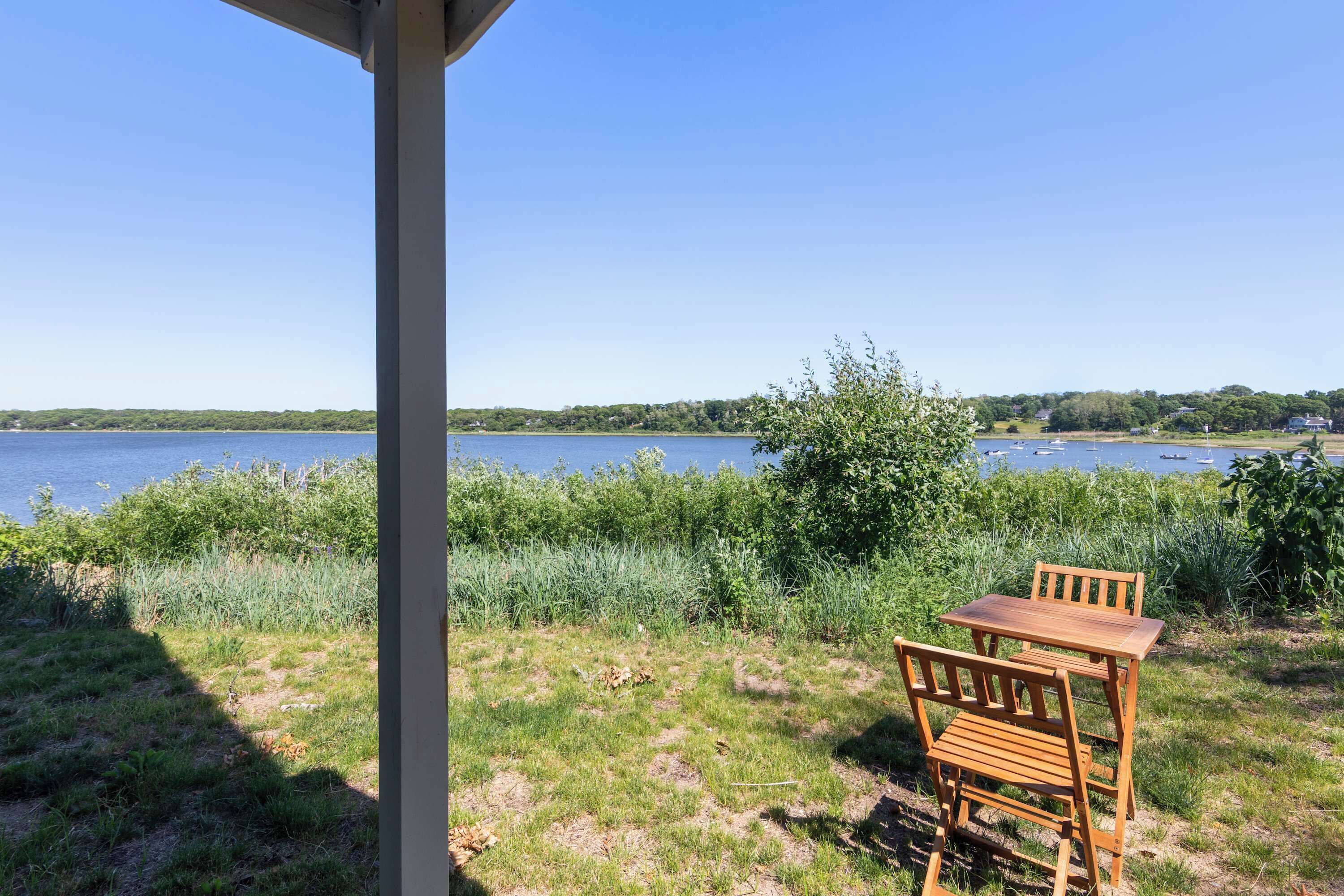 Juego de mesa y sillas de madera sobre un césped con vistas a un lago bajo un cielo despejado.