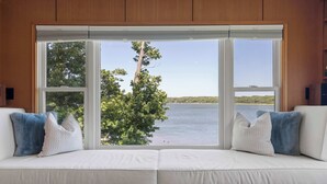 Une pièce dotée d’une grande fenêtre, d’un canapé blanc avec des coussins et offrant une vue sur une étendue d’eau et des arbres.