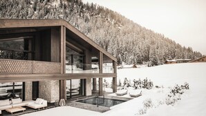 Une maison moderne dotée d’un grand balcon en verre, d’une piscine et surplombant un paysage enneigé.