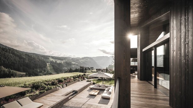 Un espace de détente extérieur moderne, doté d’une terrasse en bois, de sièges et offrant une vue sur un paysage montagneux.