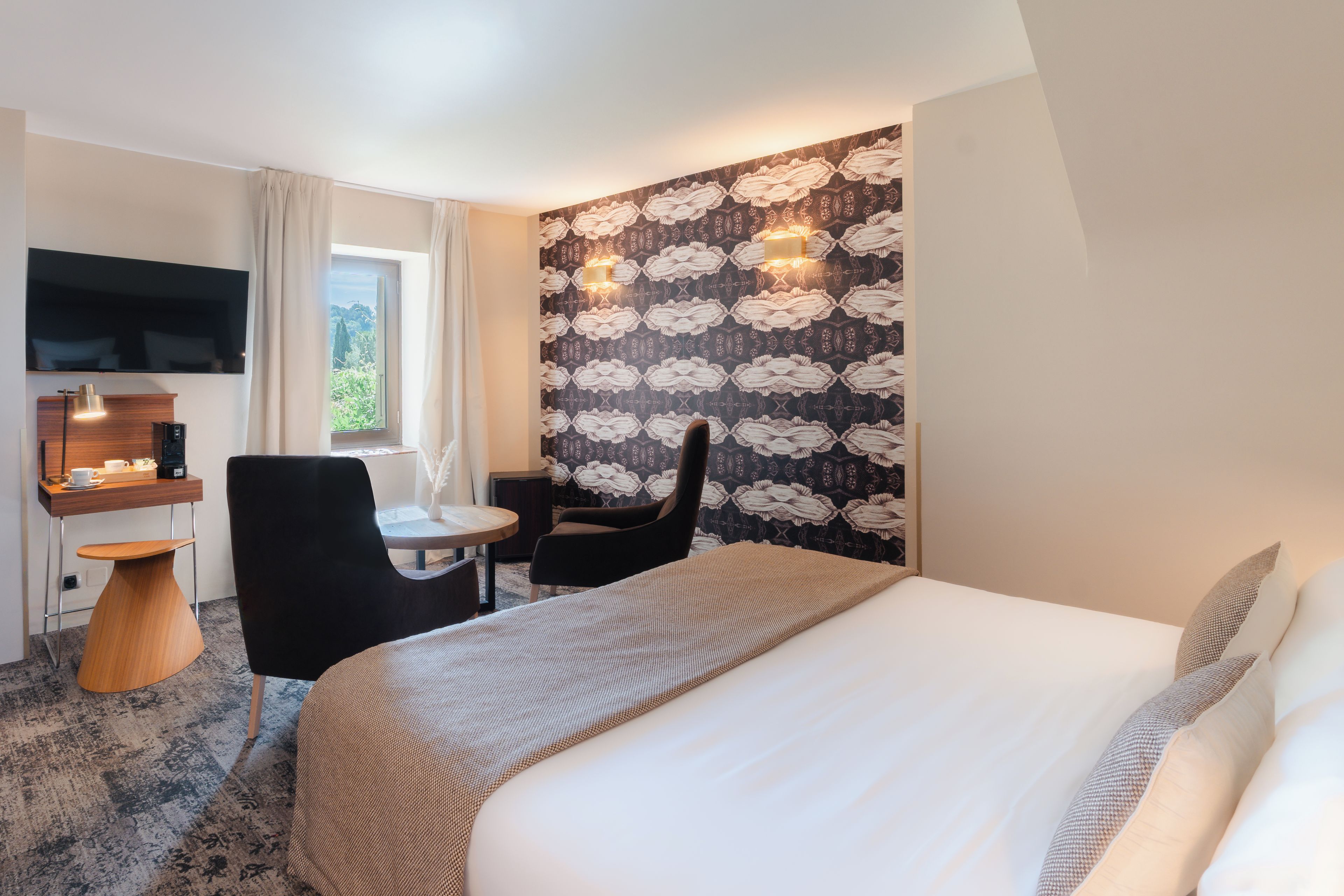 A hotel room with a bed, a desk, a chair, a TV, and a window with curtains.