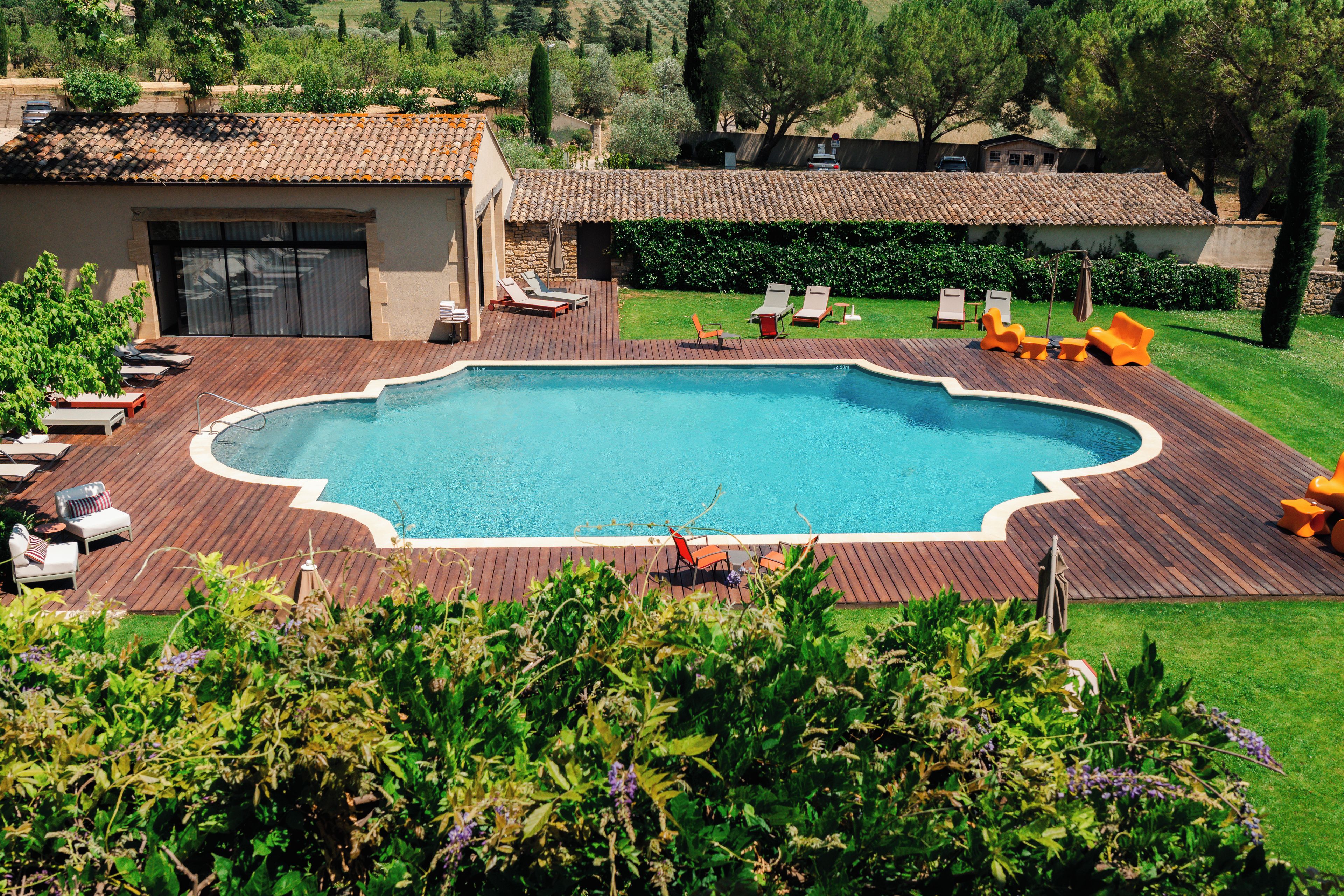 A rectangular swimming pool with a wooden deck surrounding it, equipped with multiple lounge chairs and a small table.