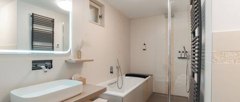 A modern bathroom with a large sink, mirror, and a walk-in shower.