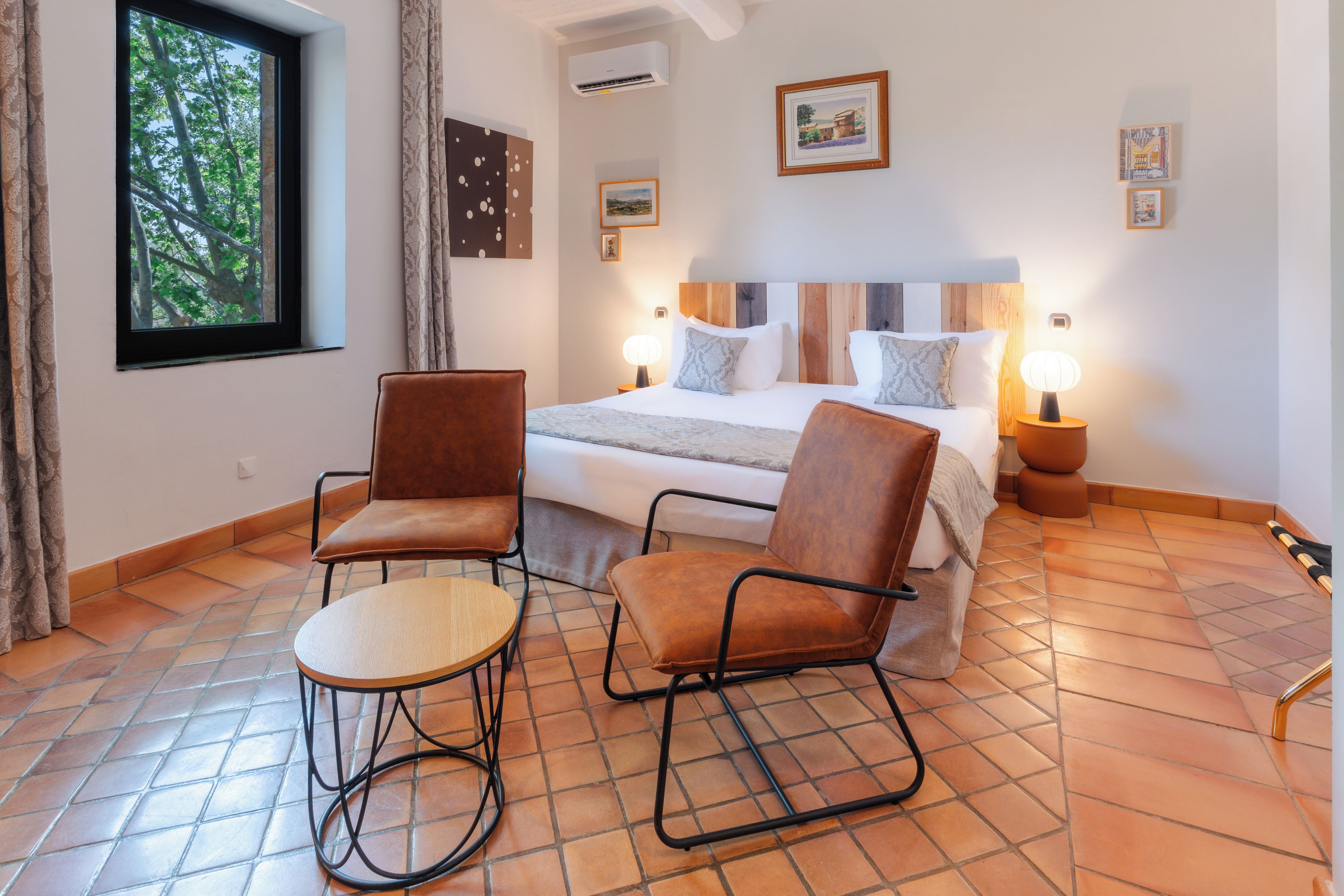 Ein Schlafzimmer mit einem Bett, zwei Stühlen, einem Tisch und einem Fenster mit Vorhängen.
