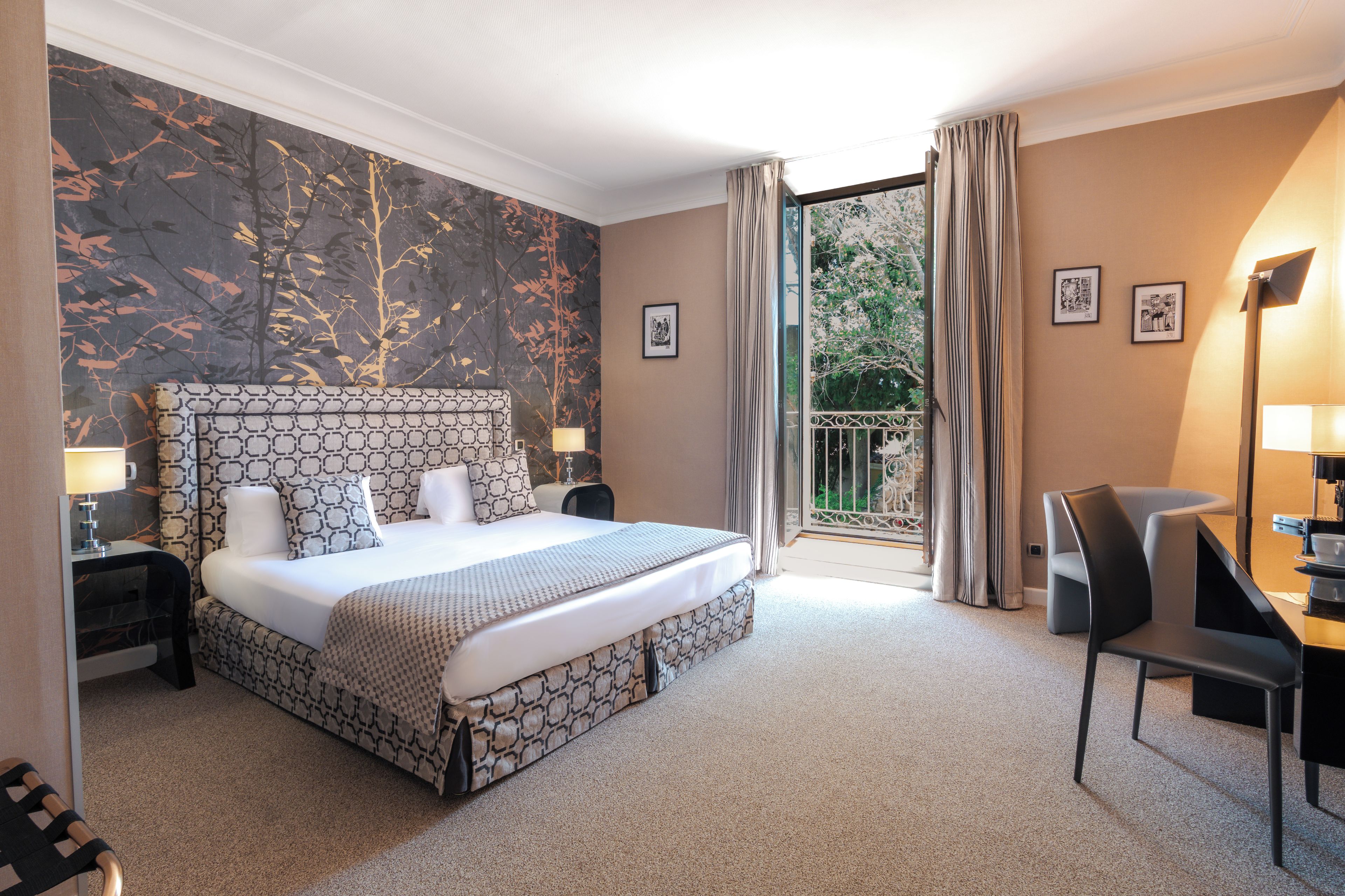 Habitación de hotel con una cama grande, un escritorio con silla, un ventanal con cortinas y una pared con diseño decorativo.