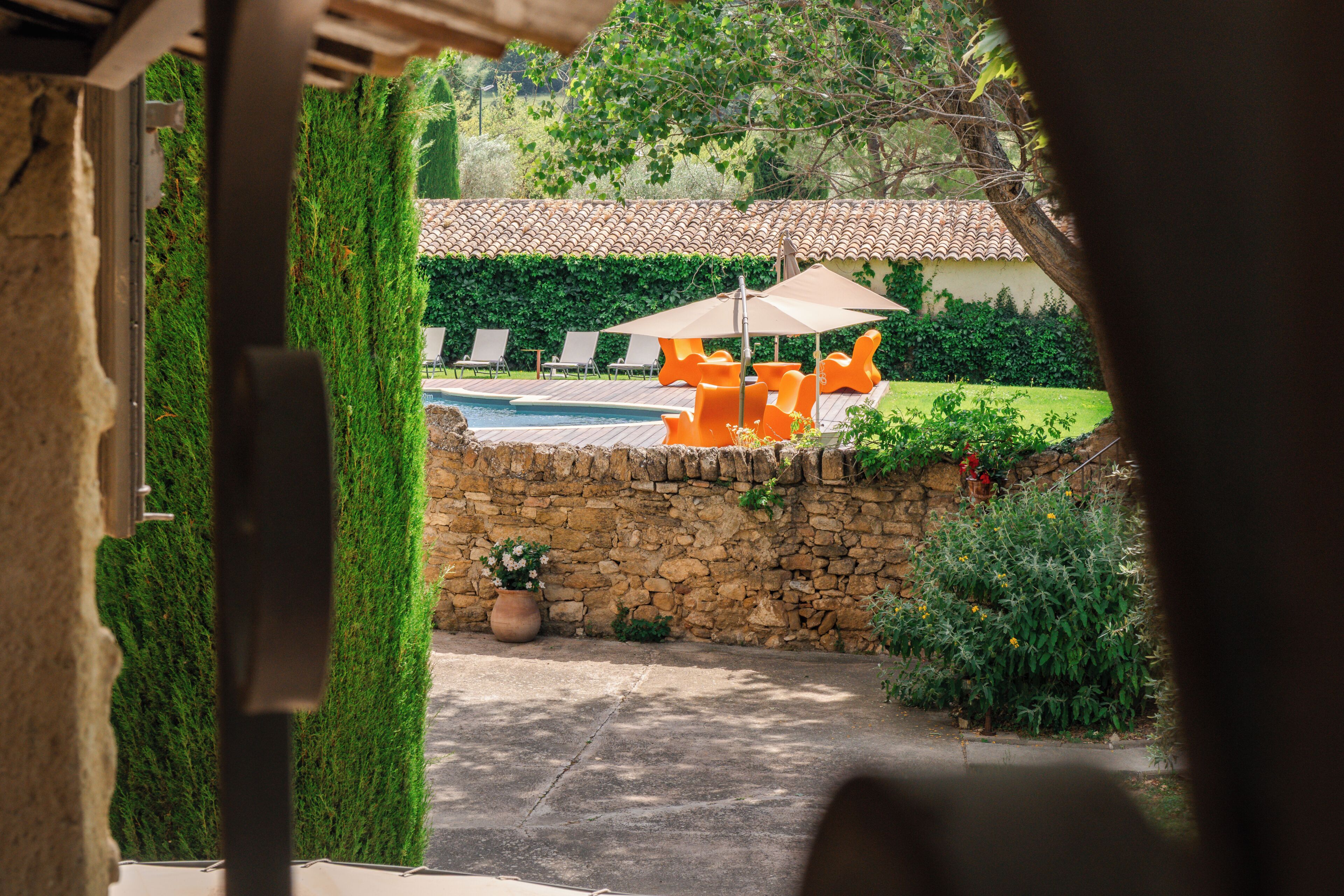 A stone wall, a swimming pool, and orange lounge chairs with umbrellas.