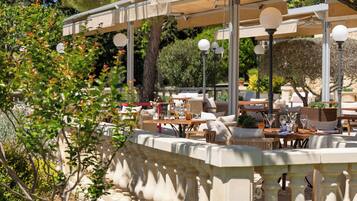 An outdoor café with tables and chairs, surrounded by greenery and a stone balustrade.