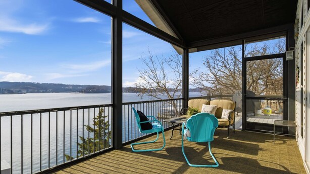 Un balcone coperto con vista su un lago, arredato con due sedie e un tavolino.