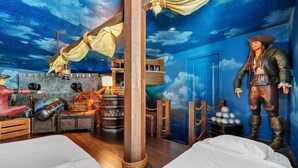 A pirate-themed room with a wooden floor, a bed, a desk with a lamp, a barrel labeled "GUN POWDER", and a large pirate statue. - Spacious Home near Disney: Private Pool, Game & Theme Rooms - 7706GR (Kissimmee)