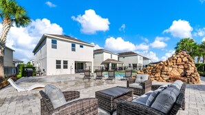A residential area with a swimming pool, outdoor furniture, and a stone structure. - Spacious Home near Disney: Private Pool, Game & Theme Rooms - 7706GR (Kissimmee)