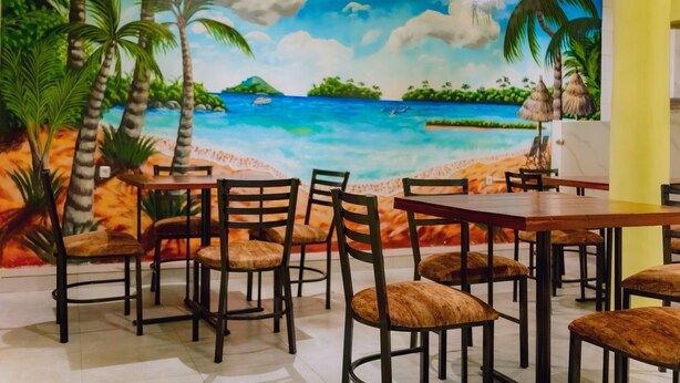 A restaurant with a mural of a beach scene, wooden tables, and cushioned chairs. - Igiraneza Apartment (Gisenyi)