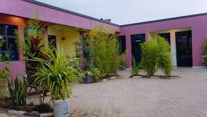 A building with a pink facade, potted plants, and a paved courtyard. - Igiraneza Apartment (Gisenyi)