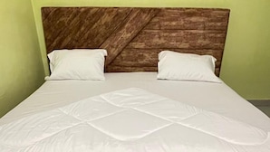 A bed with a wooden headboard, white bedding, and a green wall. - Igiraneza Apartment (Gisenyi)