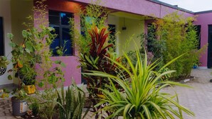 A building with a pink exterior and a paved entrance area with various potted plants. - Igiraneza Apartment (Gisenyi)