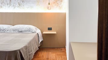 A bedroom with a bed, a hanging light, a wooden shelf, and a view of trees through a window.