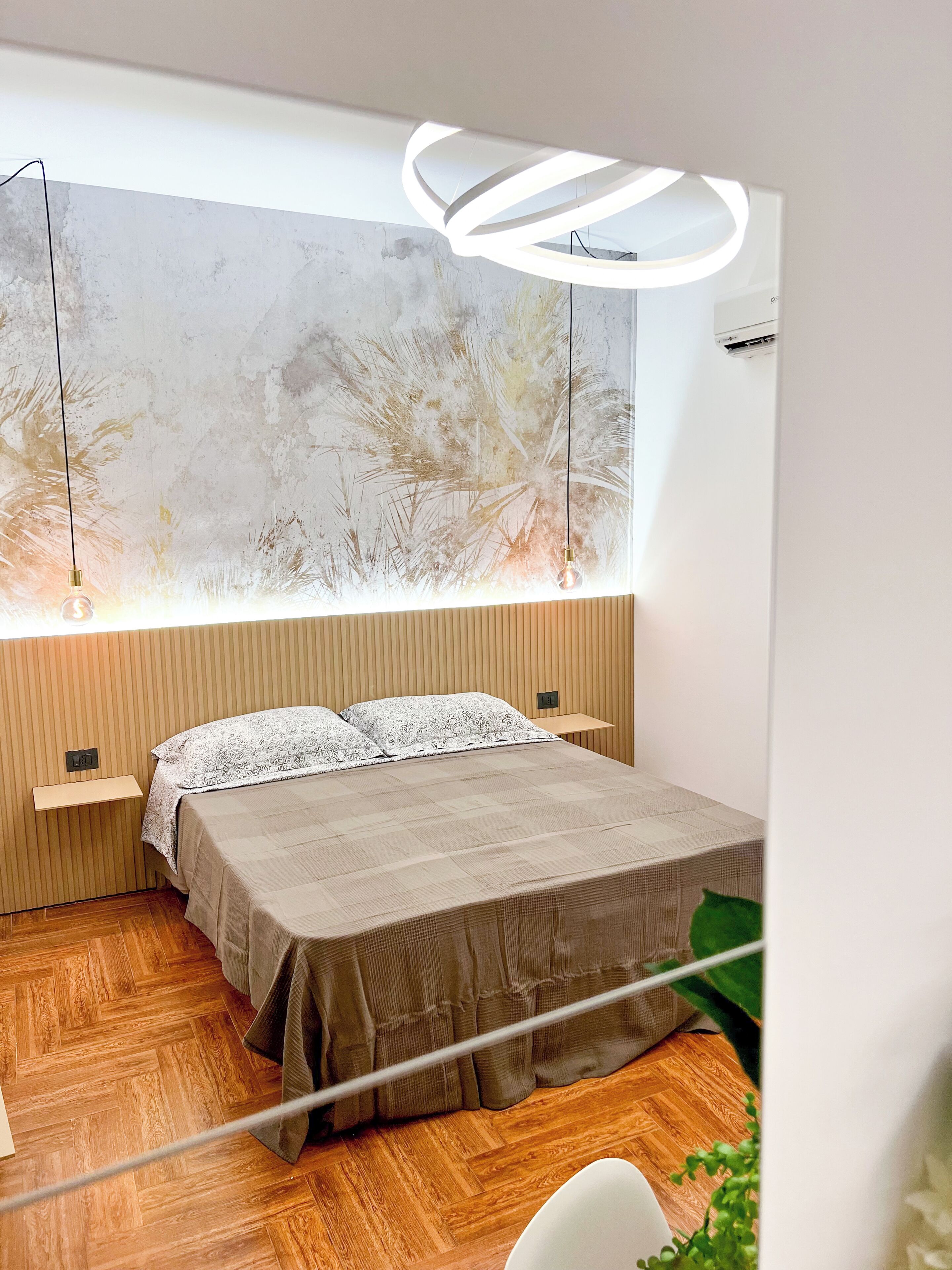 A modern bedroom with a large bed, wooden paneling, a wall-mounted light fixture, and a large abstract painting.