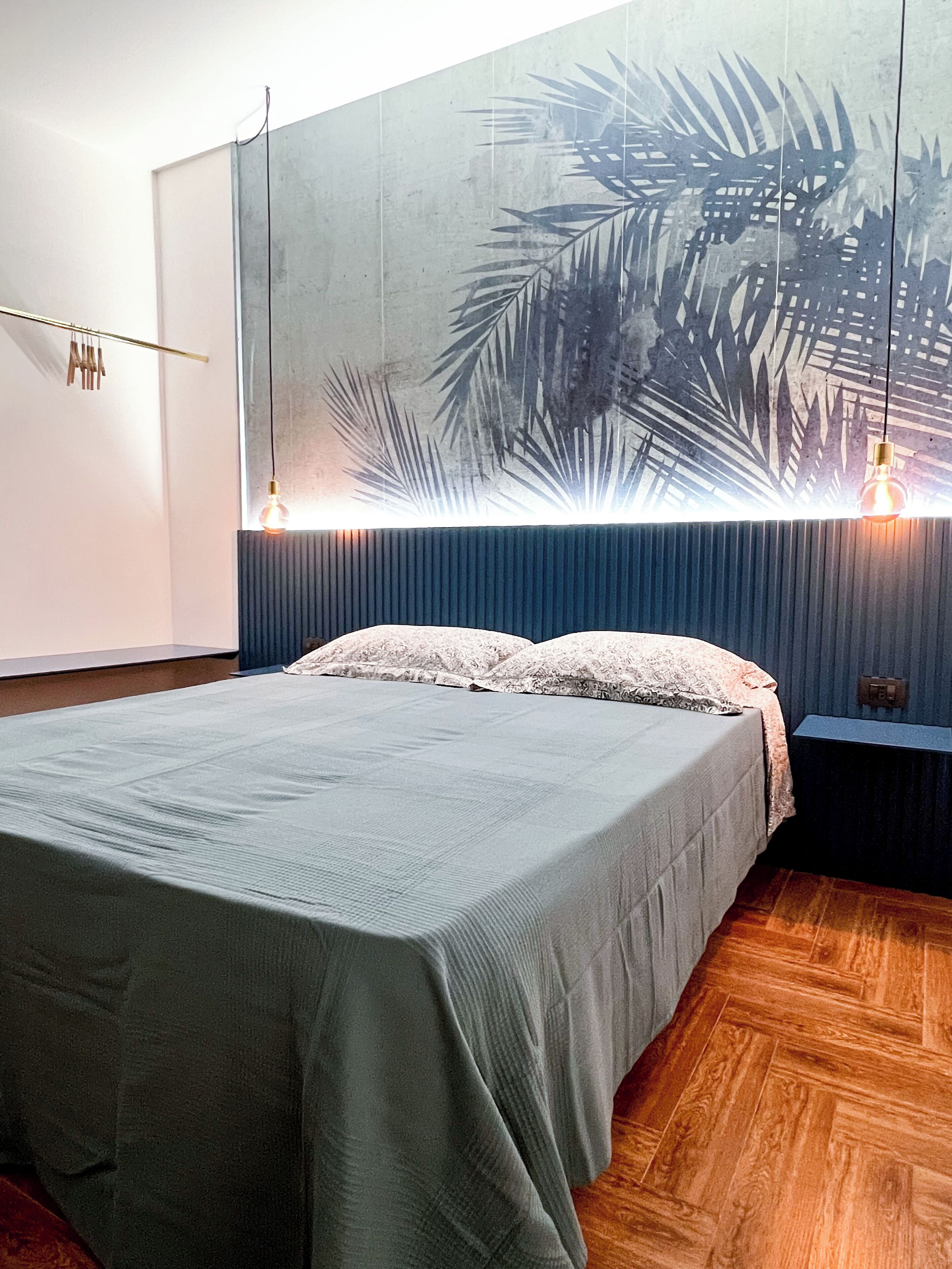 A bedroom with a bed, a wall-mounted light fixture, and a large wall art piece.
