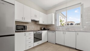Eine moderne Küche mit weißen Schränken, einem Edelstahl-Kühlschrank, einer Mikrowelle, einem Backofen und einem Geschirrspüler.