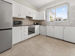 Eine moderne Küche mit weißen Schränken, einem Edelstahl-Kühlschrank, einer Mikrowelle, einem Backofen und einem Geschirrspüler.