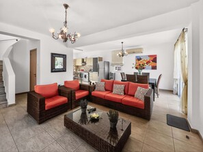 Een moderne woonkamer met een hoekbank, een glazen salontafel en een eethoek op de achtergrond.