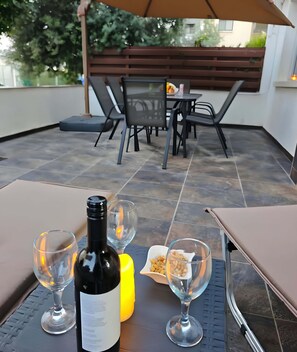 Een terras buiten met een tafel gedekt voor twee personen, een fles wijn en twee glazen.