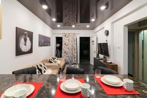 Een moderne woonkamer met een bank, een eettafel gedekt met borden en glazen, en een televisie op een dressoir.