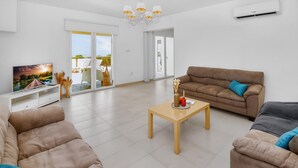 Una sala de estar moderna con un sofá, una mesa de centro, un televisor y un ventanal corredero que da a un balcón.